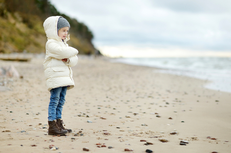 Adorable little girl looking at ocean on cold winter dayの写真素材