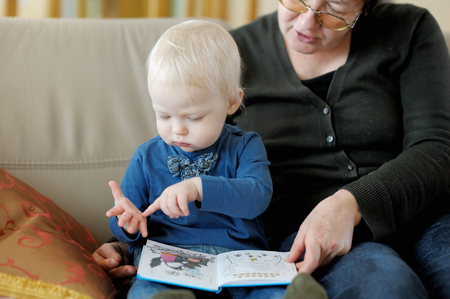Grandmother and toddler granddaughter reading a book togetherの写真素材