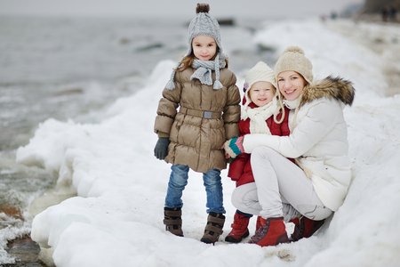 Young mother and her two daughters by the sea on winterの写真素材