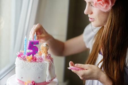 Young mother decorating her daughters birhtday cakeの写真素材