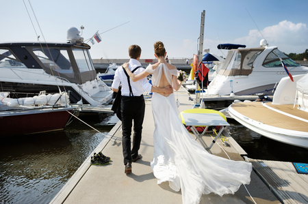 Happy bride and groom walking on pier in small harborの写真素材