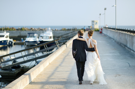 Happy bride and groom walking on pier in small harborの写真素材