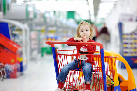 Adorable toddler girl sitting in shopping cartの写真素材