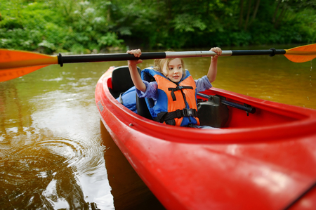 Happy little girl on a kayak on a river at summerの写真素材