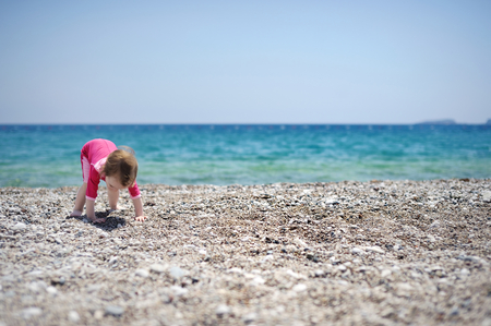 Cute toddler girl playing on a pebble beachの写真素材