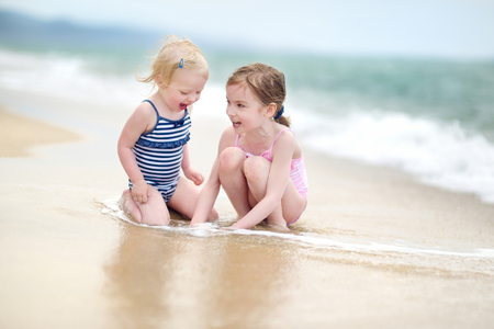 Two little sisters having fun on a sandy beachの写真素材