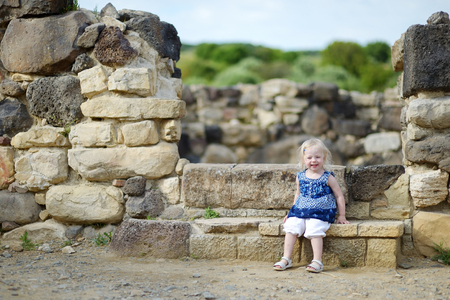 Little girl sightseeing historical ruins of Nuraghi villageの写真素材