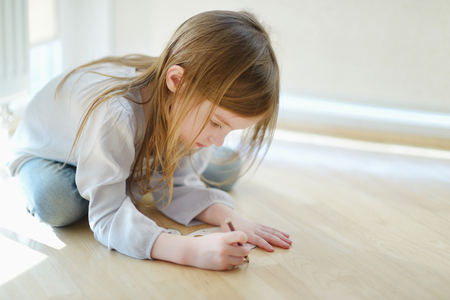 Cute little girl is drawing with pencils on the floorの写真素材