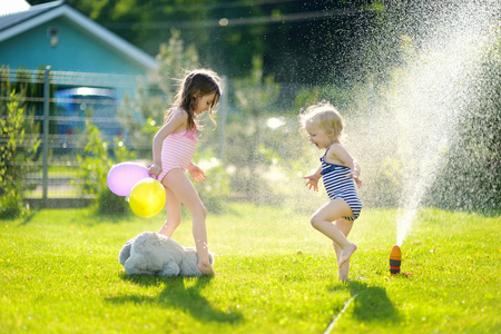 Little girls running though a sprinkler in a backyardの写真素材