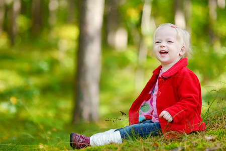 Adorable toddler girl sitting in the forest on autumn dayの写真素材