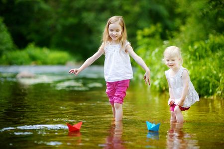 Two adorable little sisters playing with paper boats in a riverの写真素材