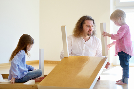 Happy father and his two daughters assembling a table togetherの写真素材