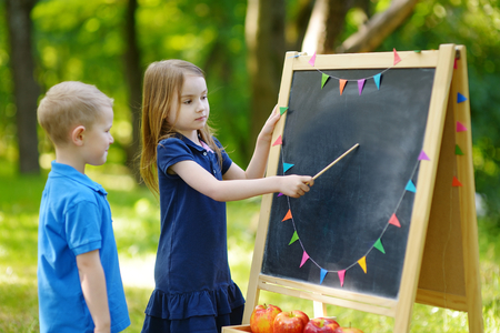 Adorable little girl playing a teacher standing by a blackboard in front of her little studentの写真素材