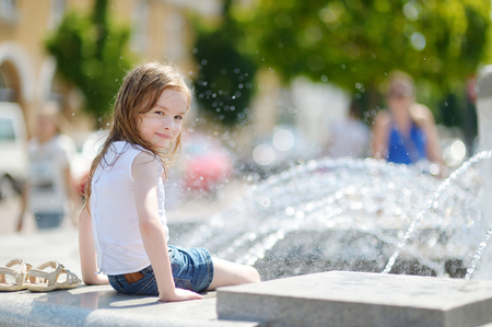 Cute little preschooler girl playing with a city fountain on hot and sunny summer dayの写真素材