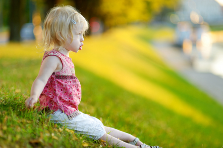 Cute little girl toddler sitting on the grass on a sunny summer dayの写真素材