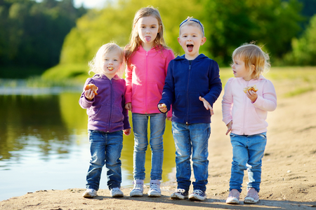 Three little sisters and their brother eating buns, laughing and joking by a river at sunny autumn dayの写真素材