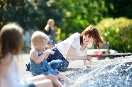 Young woman and two little kids having fun by a city fountain on hot and sunny summer dayの写真素材