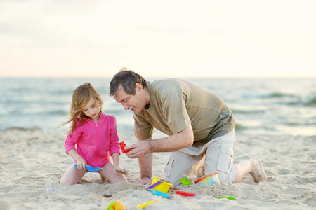 Adorable little girl wearing pink jacket playing on a beach at cold summer dayの写真素材