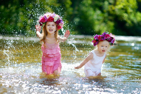 Two adorable little sisters wearing flowers crowns having fun by a river on warm and sunny summer dayの写真素材