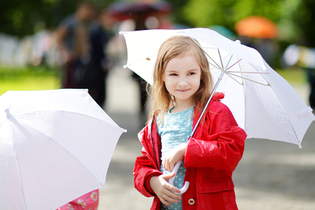 Adorable little girl holding white umbrella at rainy day in autumnの写真素材