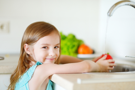 Adorable little girl washing vegetables in a kitchenの写真素材