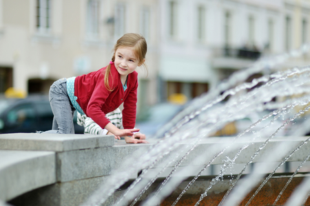 Cute little preschooler girl playing with a city fountain on a warm summer dayの写真素材