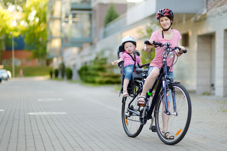 Young mother and her cute little toddler daughter in a child seat getting ready to ride a bicycleの写真素材
