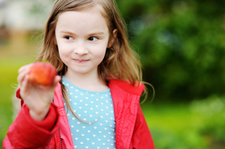 Cute little preschooler girl holding a ripe strawberry on beautiful autumn dayの写真素材