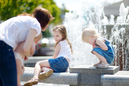 Young woman and three little kids having fun by a city fountain on hot and sunny summer dayの写真素材