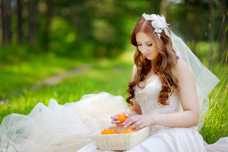Young beautiful bride sitting on a grass in beautiful summer parkの写真素材