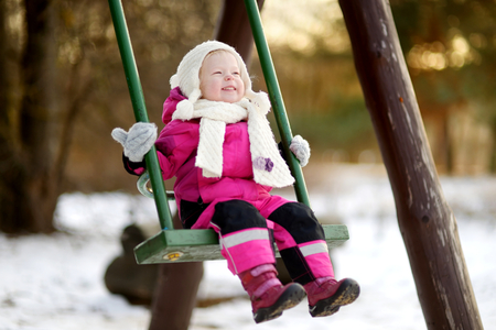Adorable girl having fun on a swing on beautiful winter dayの写真素材