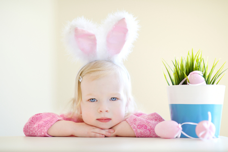 Adorable toddler girl wearing bunny ears playing with colorful Easter eggsの写真素材