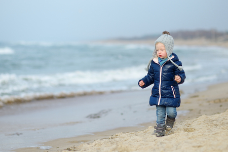 Adorable little girl playing by the ocean on cold winter dayの写真素材