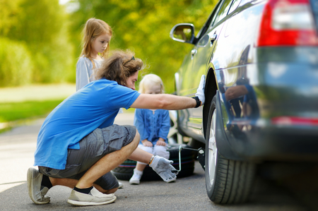 Young father and his two daughters changing a car wheel outdoors on beautiful summer dayの写真素材