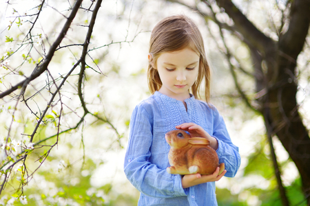 Adorable little girl in blooming cherry garden holding easter bunny on beautiful spring dayの写真素材