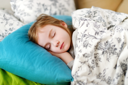 Adorable little girl sleeping in a bedの写真素材