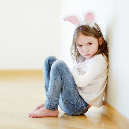 Very angry little girl wearing bunny ears sitting on a floor at homeの写真素材