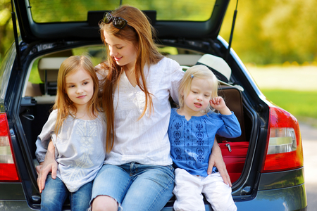 Two adorable little sisters and their mother sitting in a car just before leaving for a car vacationの写真素材
