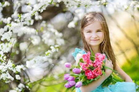 Adorable little girl holding tulips for her mother in blooming cherry garden on beautiful spring dayの写真素材