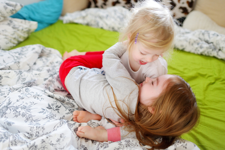 Two little sisters fooling around, playing and having fun in bed on sunny sunday morningの写真素材