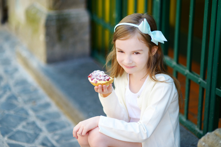 Adorable little girl eating fresh sweet strawberry cake outdoors on warm and sunny summer day in Italyの写真素材
