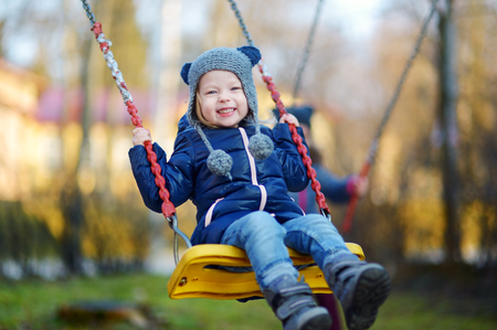 Adorable girl having fun on a swing on beautiful autumn dayの写真素材