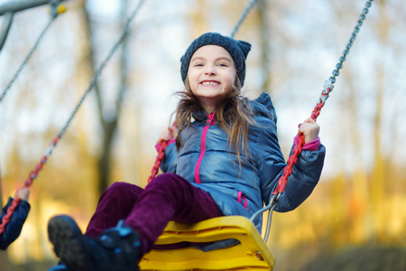 Adorable girl having fun on a swing on beautiful autumn dayの写真素材