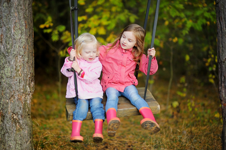 Two sisters swinging outdoors on beautiful sunny autumn dayの写真素材