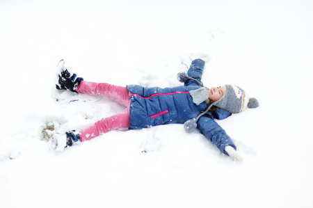 Funny little girl having fun in beautiful winter park during snowfallの写真素材