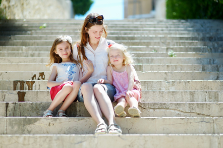 Two adorable little sisters and their mom having fun together on warm and sunny summer day in italian townの写真素材