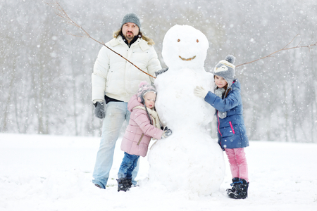 Young father and his two daughters building a snowman on winter dayの写真素材