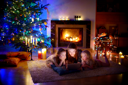 Young mother and her daughters using a tablet pc by a fireplace on warm Christmas eveningの写真素材