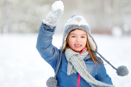 Funny little girl having fun in beautiful winter park during snowfallの写真素材