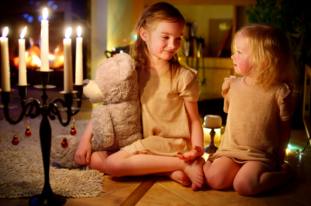 Happy little girls sitting by a fireplace in a cozy dark living room on Christmas eveの写真素材
